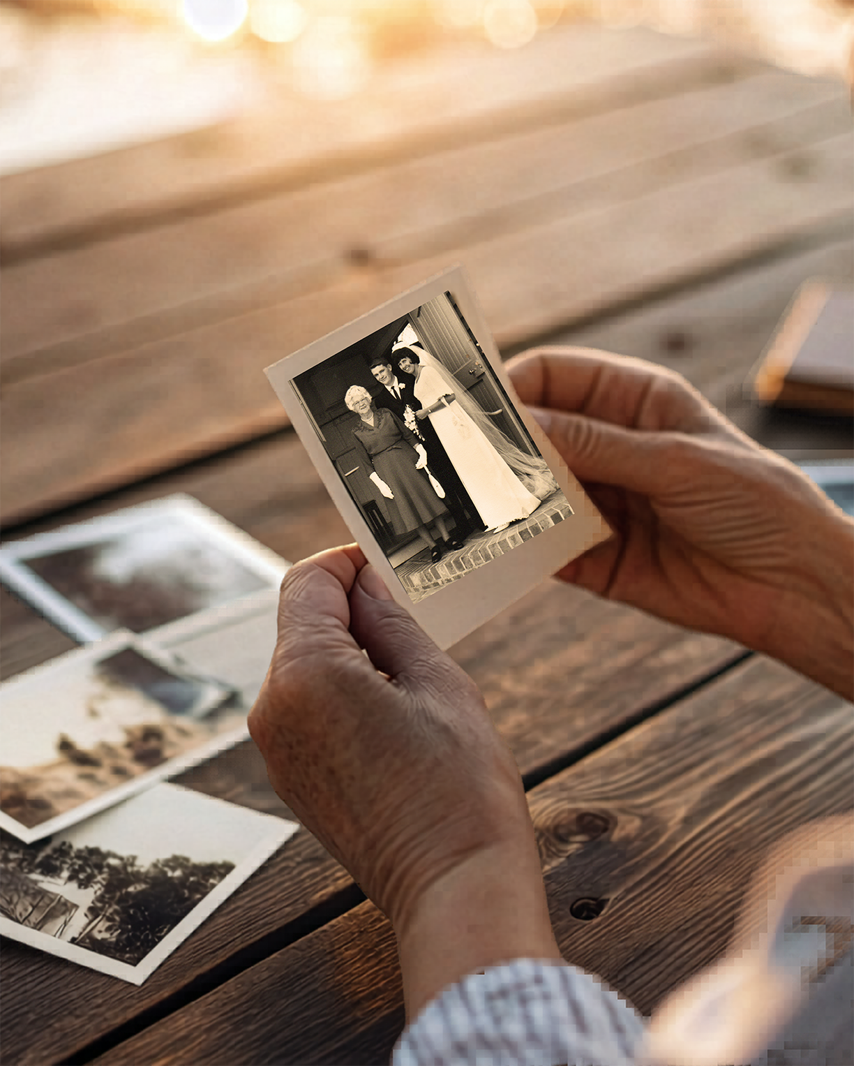 Elderly hands holding a vintage black-and-white wedding photograph, surrounded by old family photos on a warm wooden table